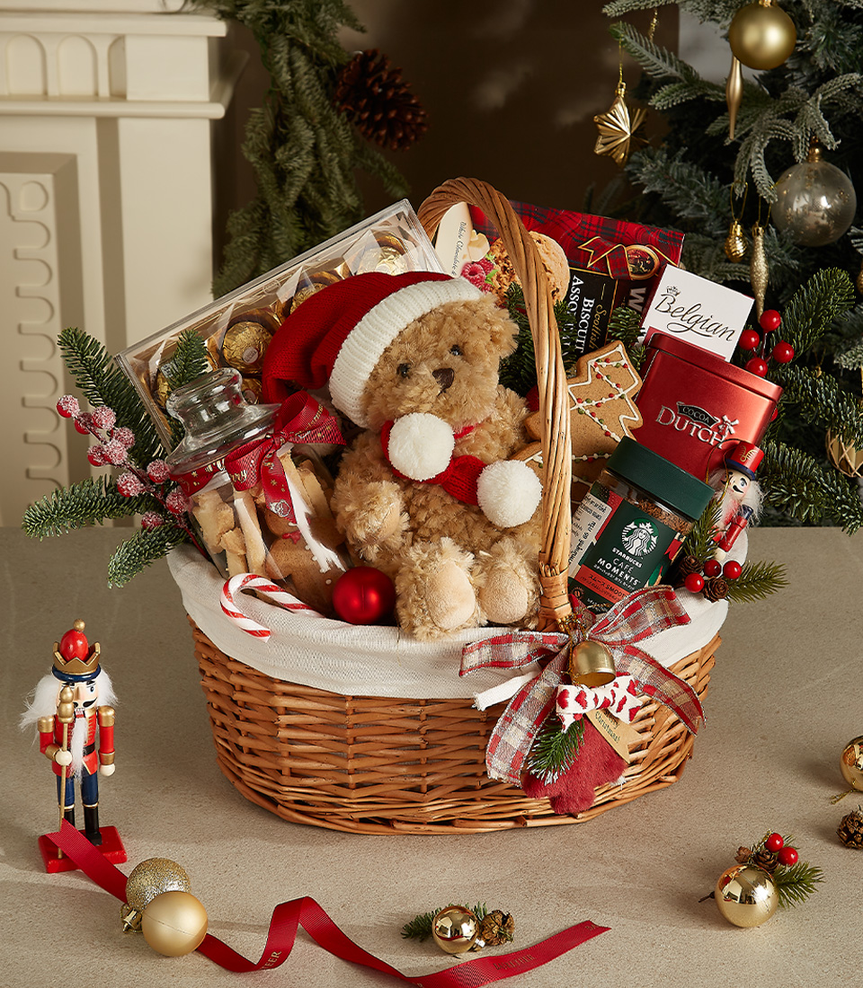 Wicker gift basket with a Santa teddy bear, Belgian chocolates, gingerbread, festive cookies, Starbucks coffee, and holiday decorations.