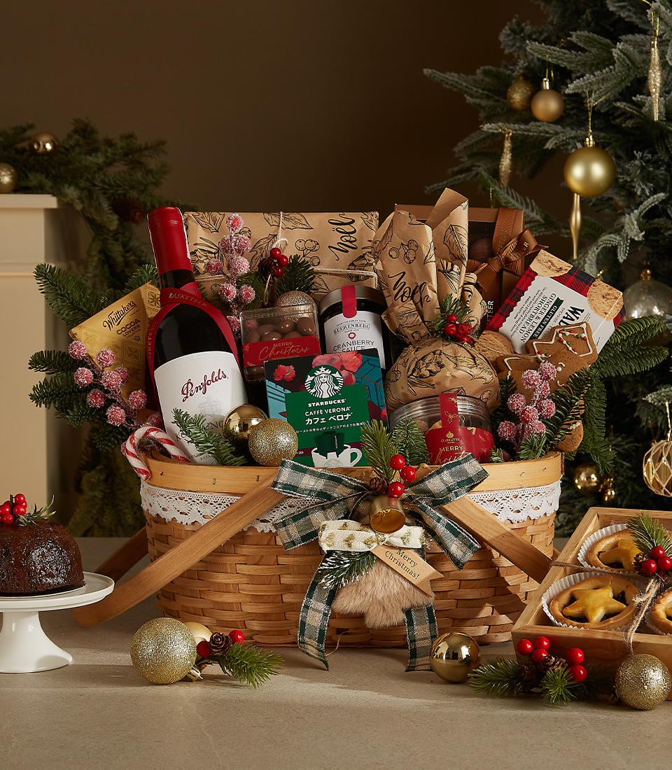 Christmas hamper with red wine, plum pudding, fruit pies, coffee, and holiday-themed treats in a decorated wicker basket.