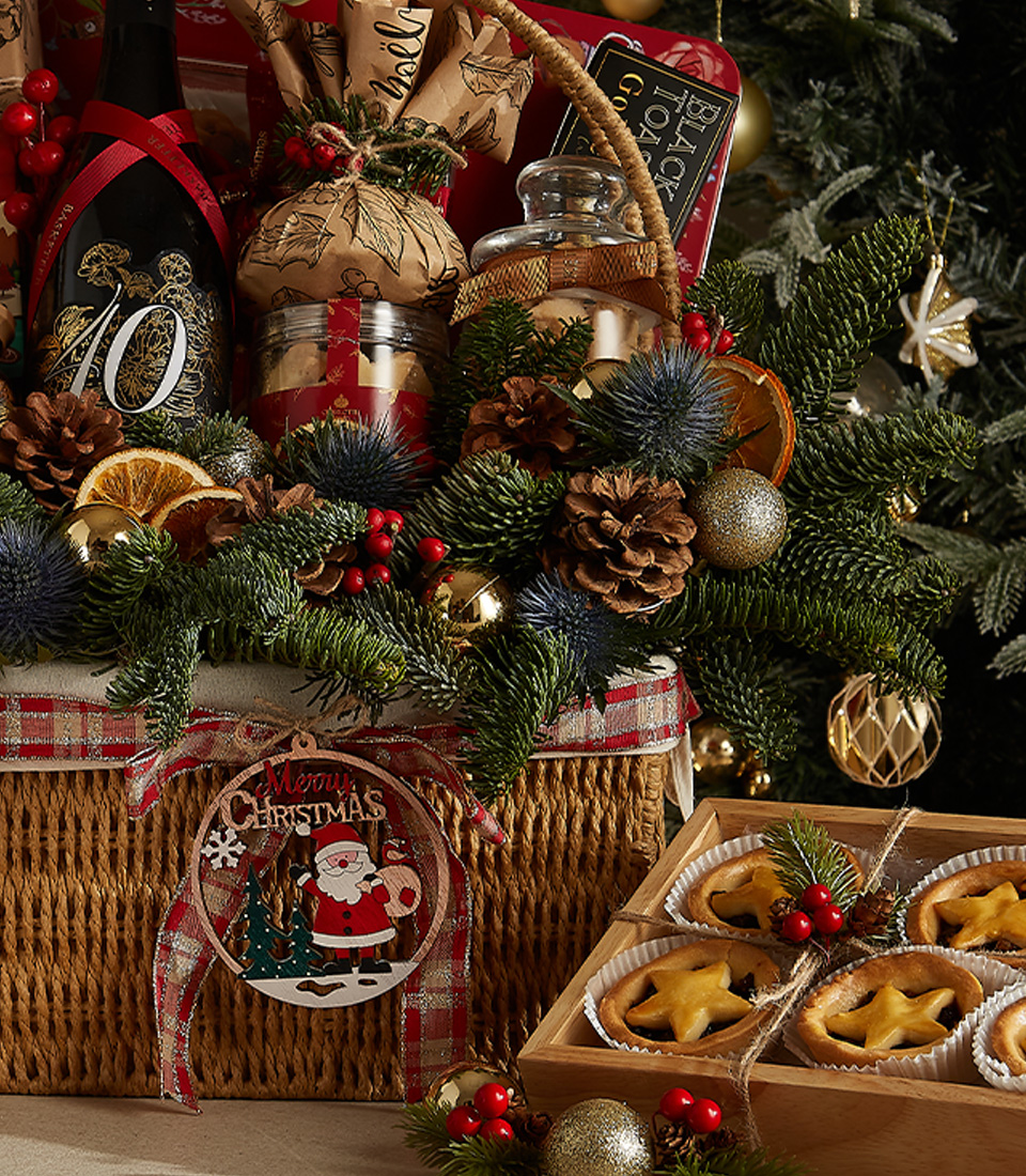 Luxurious Christmas hamper with red wine, Christmas pudding, mince pies, festive cookies, chocolates, and seasonal decorations.