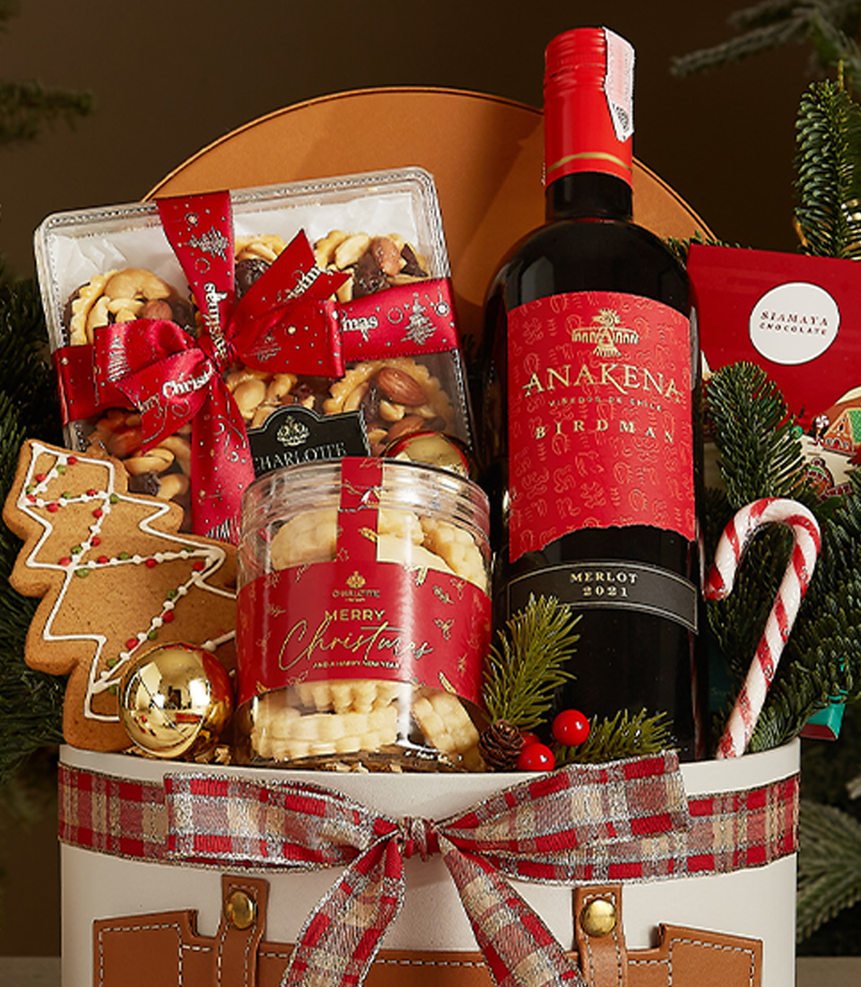 White Christmas gift box with leather accents and plaid ribbon, containing Anakena red wine, butter cookies, gingerbread, candy canes, and festive chocolates.