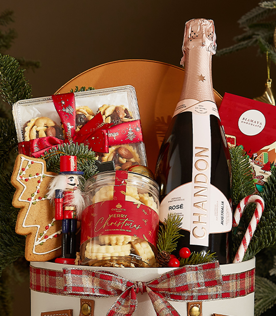 White gift box with leather accents and plaid ribbon featuring Chandon Rosé, gingerbread, butter cookies, candy canes, and holiday chocolates.