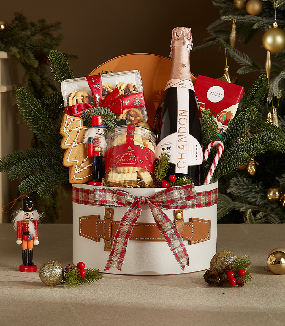 White gift box with leather accents and plaid ribbon featuring Chandon Rosé, gingerbread, butter cookies, candy canes, and holiday chocolates.