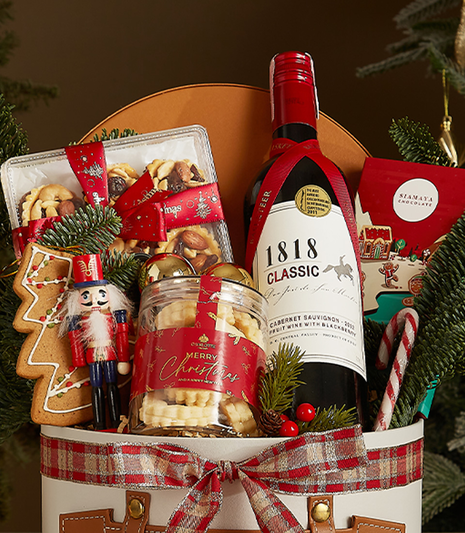 White gift box with leather accents and plaid ribbon featuring 1818 Classic Red Wine, butter cookies, gingerbread, and holiday chocolates.