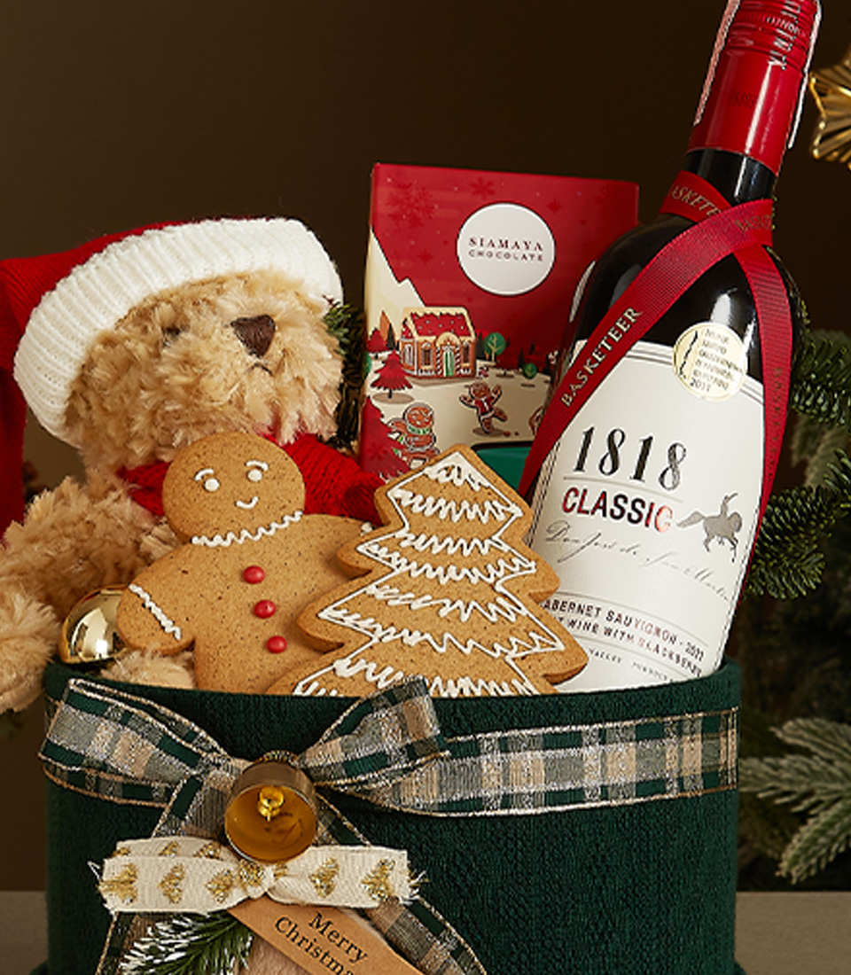Green velvet gift box with plaid ribbon, featuring a Santa hat teddy bear, red wine, gingerbread cookies, and festive holiday treats.