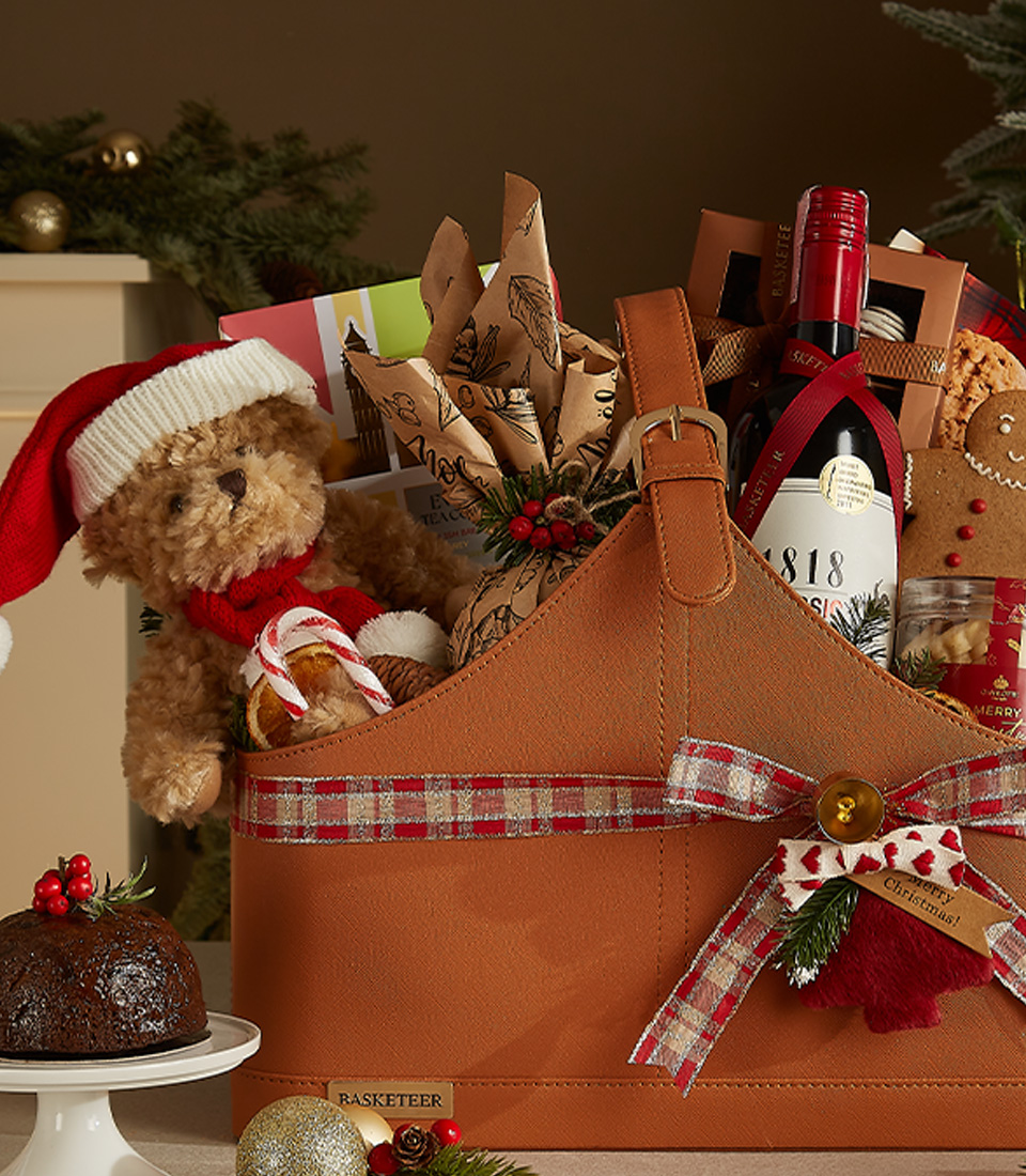 Luxurious leather Christmas gift basket featuring 1818 Classic wine, gourmet snacks, festive cookies, a plush Santa bear, and holiday decor.