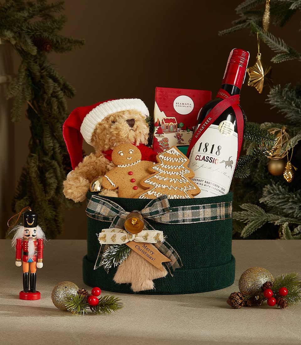Green velvet gift box with plaid ribbon, featuring a Santa hat teddy bear, red wine, gingerbread cookies, and festive holiday treats.
