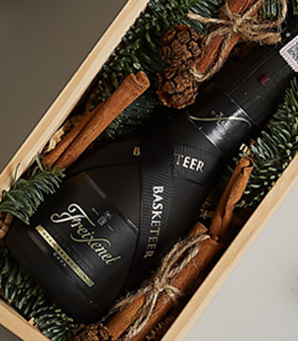 Holiday-themed gift box with Freixenet Prosecco, gingerbread cookies, and festive decorations in a wooden box.