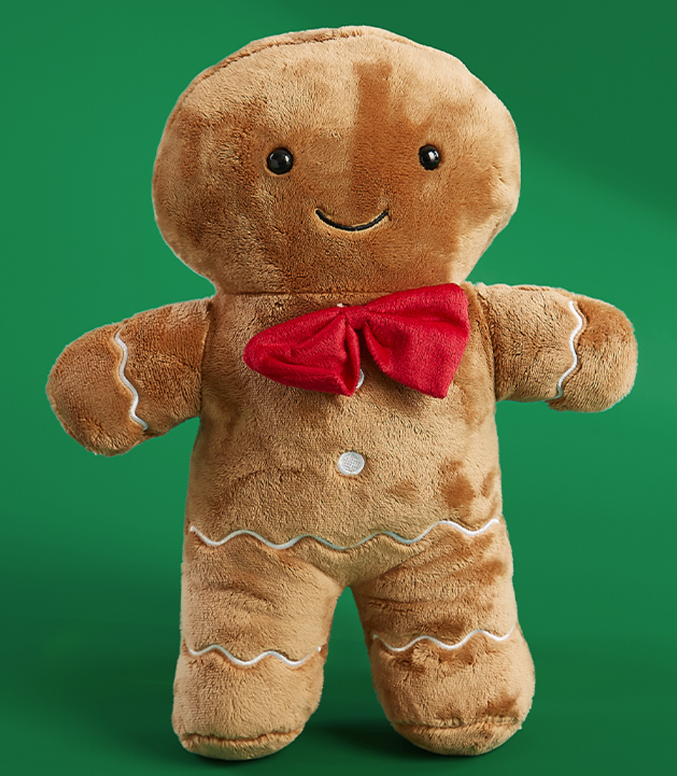 Cute plush gingerbread man doll with a red bow tie and embroidered white icing details on a green background.