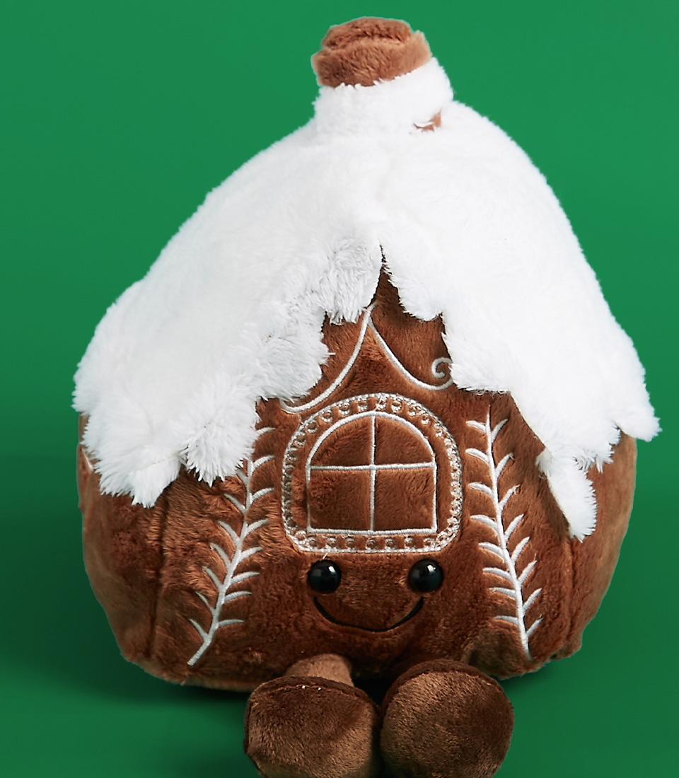 A single plush gingerbread house toy with a snow-covered roof, embroidered details, and a smile on a green background.