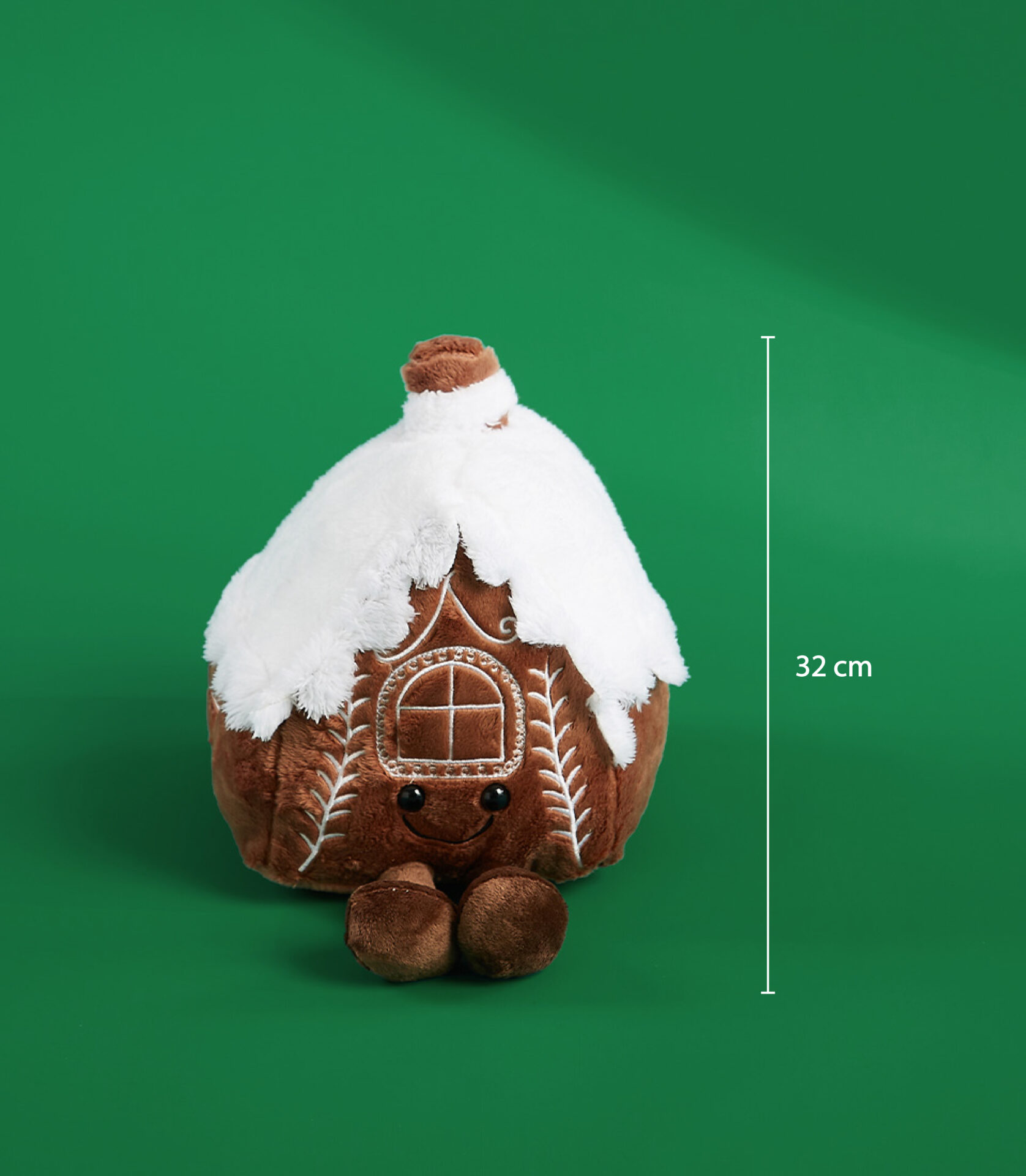 32 cm gingerbread house plush toy with a snowy roof and embroidered details on a green background.