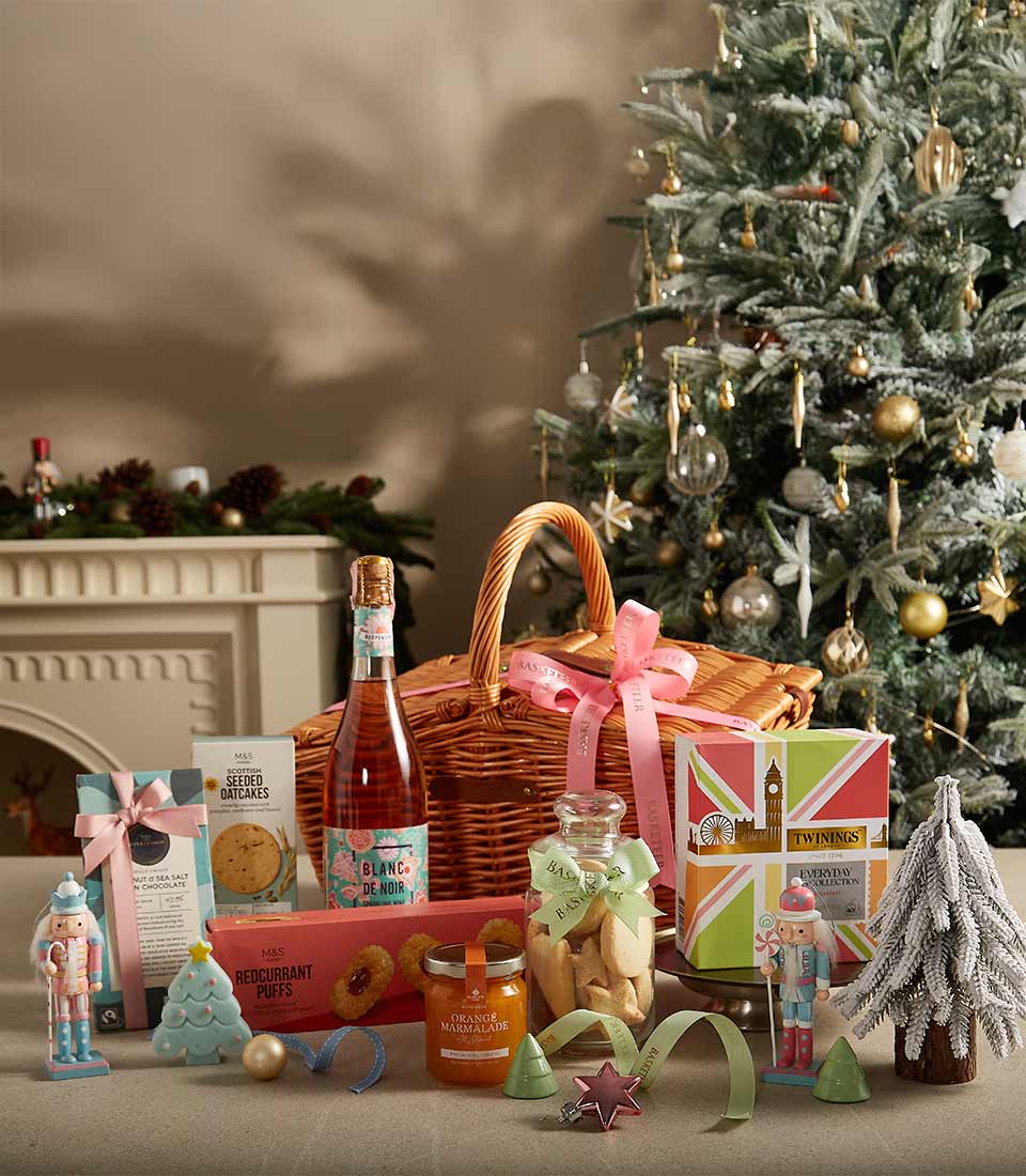 Holiday gift basket with premium tea, sparkling rosé, cookies, and festive decorations in a wicker basket.
