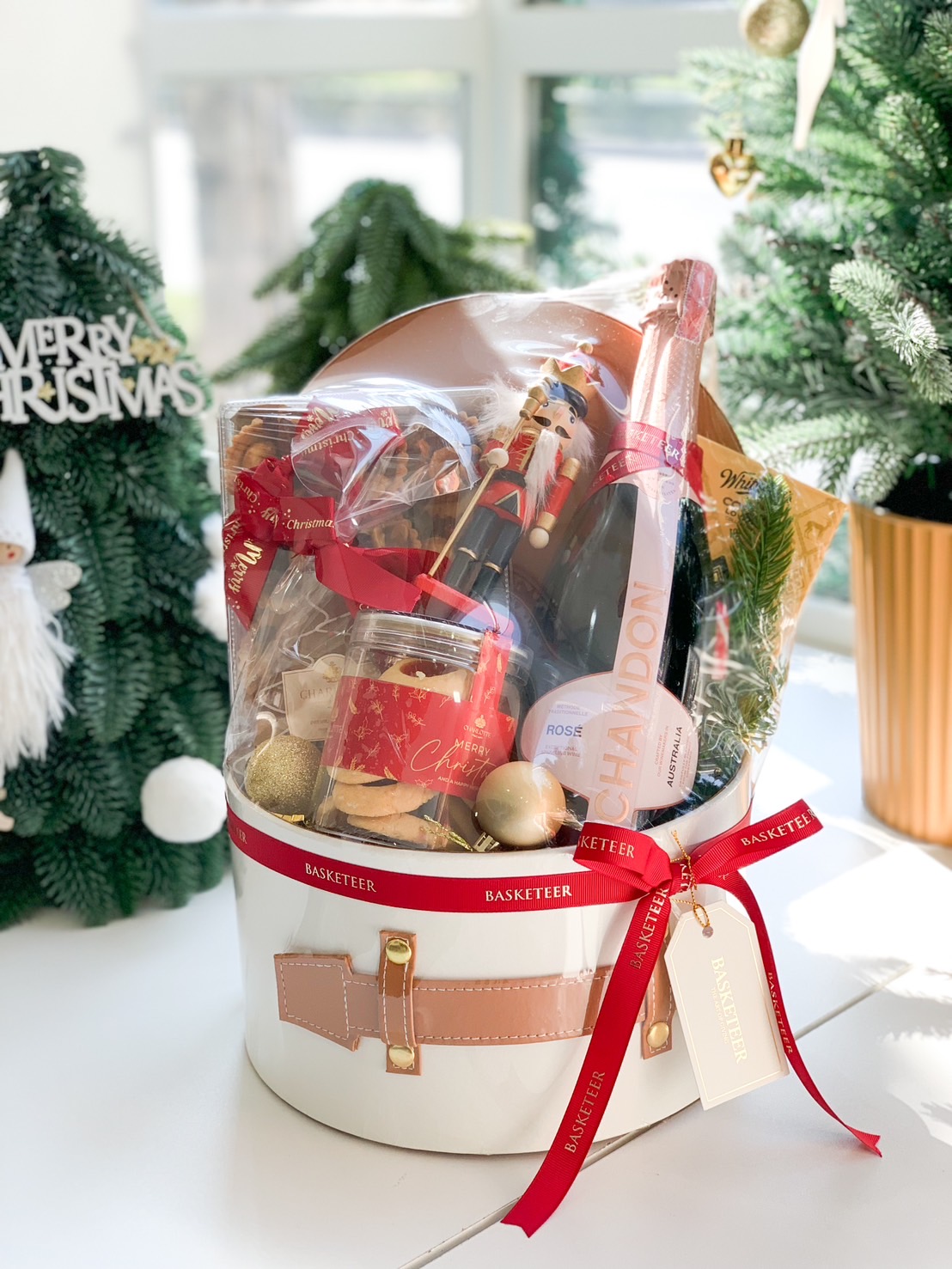 Christmas hamper in a Santa-themed bucket featuring a bottle of Chandon Rosé, cookies, a Nutcracker ornament, and festive red ribbons.