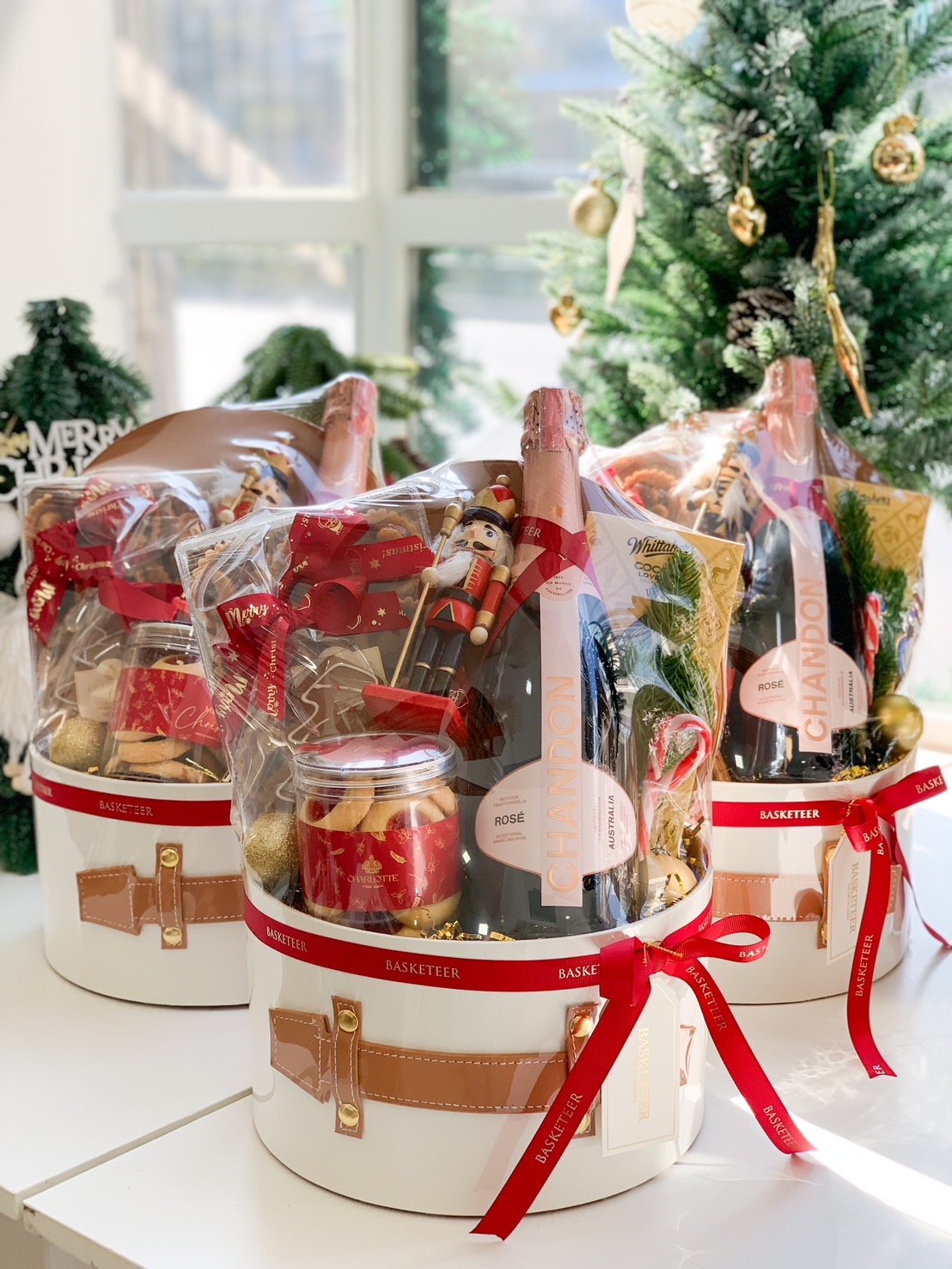 Christmas hamper in a Santa-themed bucket featuring a bottle of Chandon Rosé, cookies, a Nutcracker ornament, and festive red ribbons.