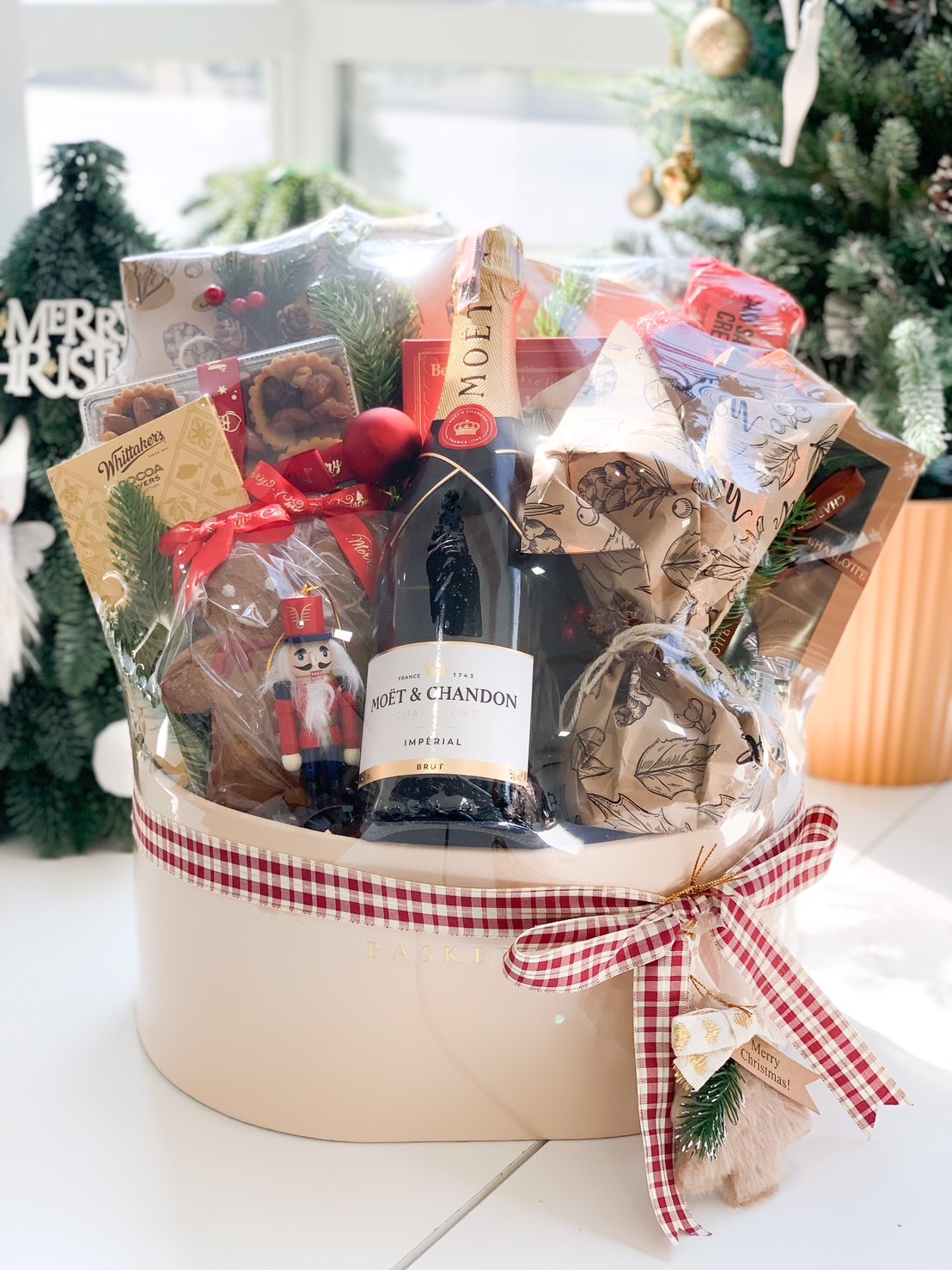 A luxurious holiday gift hamper with festive treats, chocolates, and a sparkling bottle, decorated with red and white ribbons.