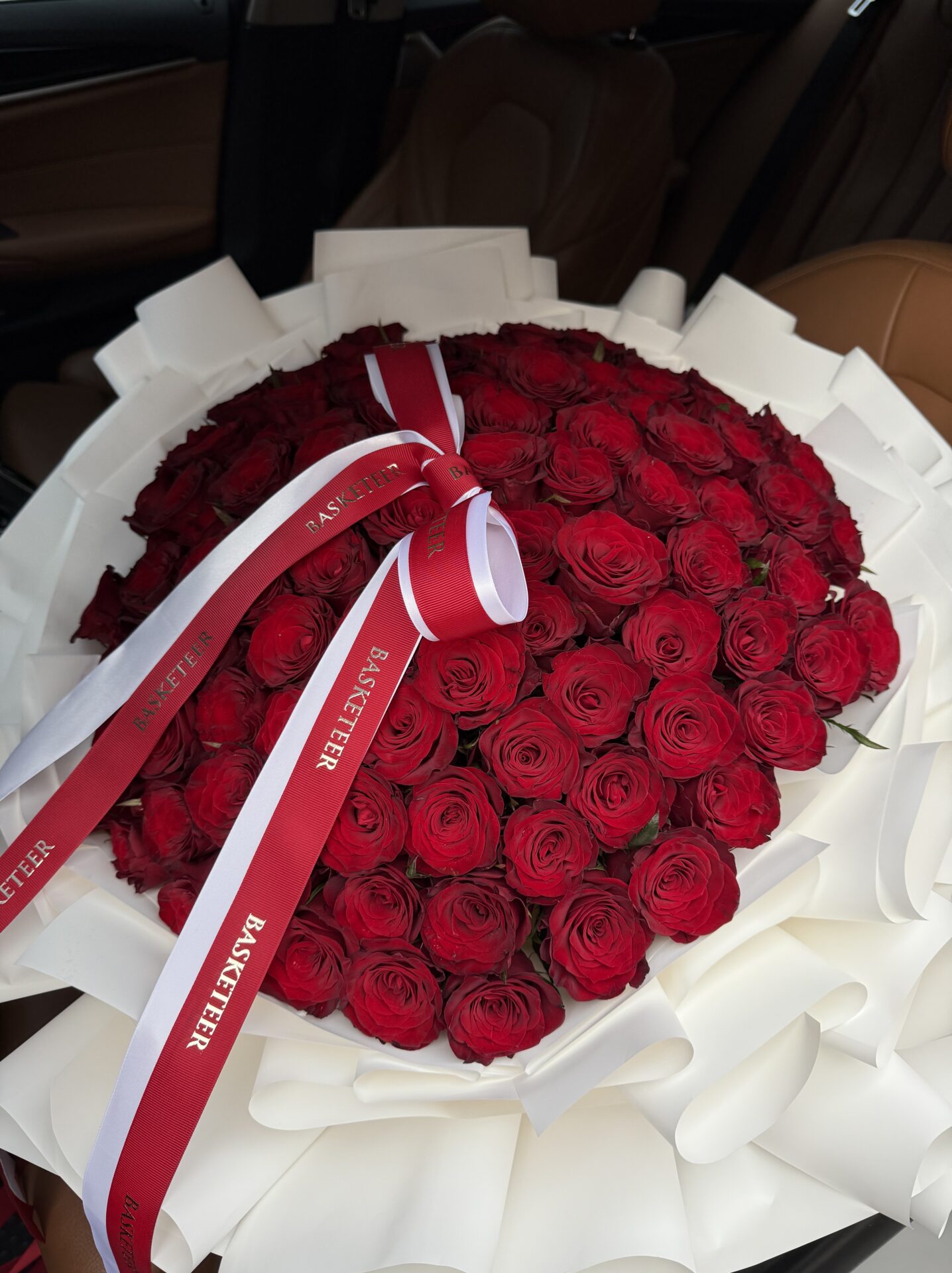 Extravagant bouquet of luxury red roses wrapped in white paper, tied with elegant red and white Basketeer ribbons.