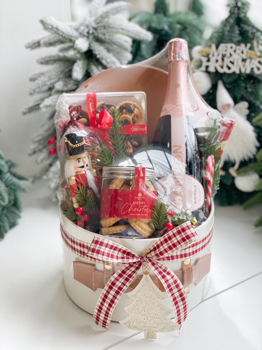 White gift box with leather accents and plaid ribbon featuring Chandon Rosé, gingerbread, butter cookies, candy canes, and holiday chocolates.