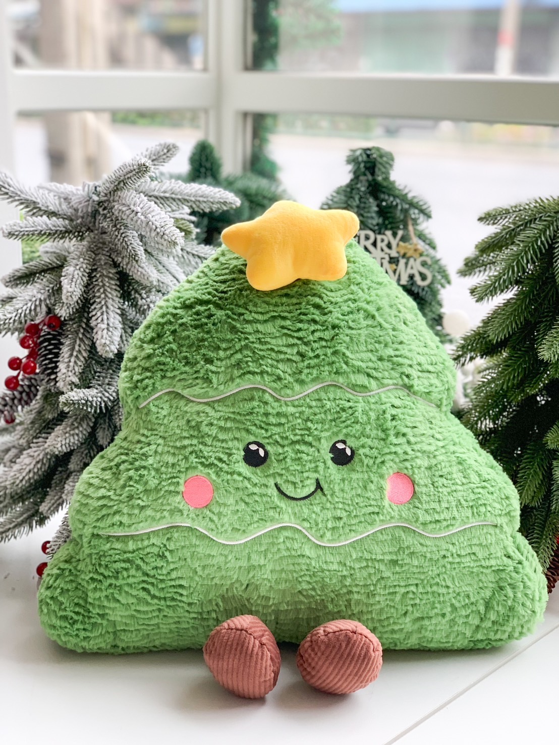 Plush Christmas tree pillow with a star topper, smiling face, and soft green texture.