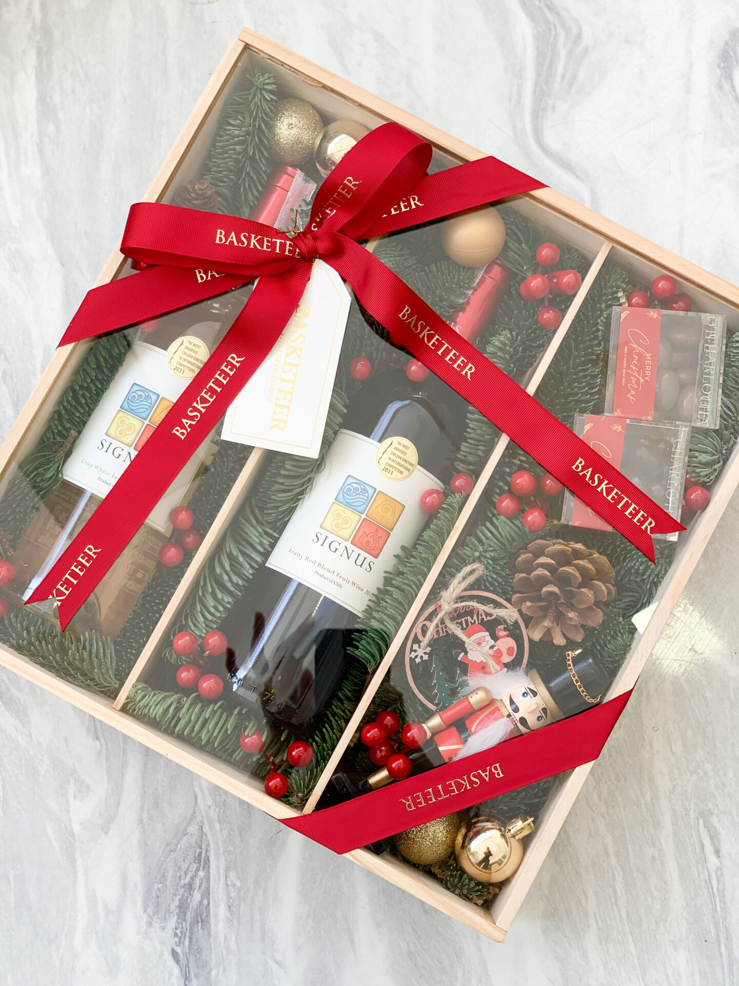 Christmas gift box with red and white Signus wines, chocolates, nutcracker, and holiday decorations.
