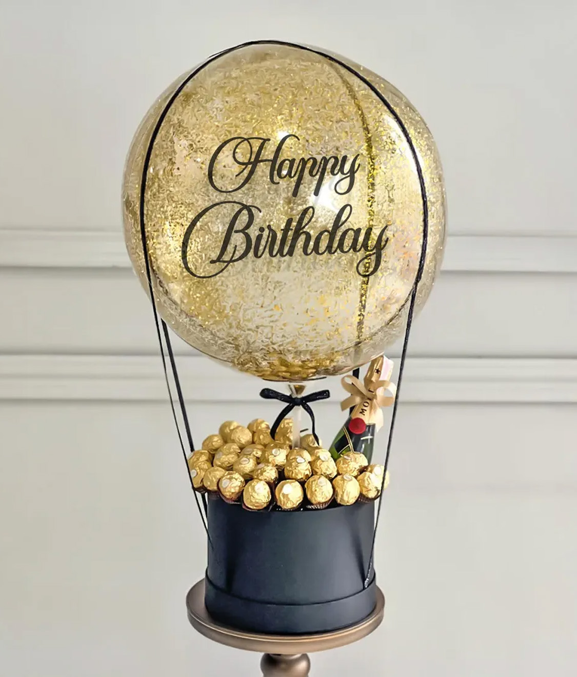 Elegant birthday gift featuring a gold balloon with 'Happy Birthday' text, Ferrero Rocher chocolates, and a stylish black gift box.