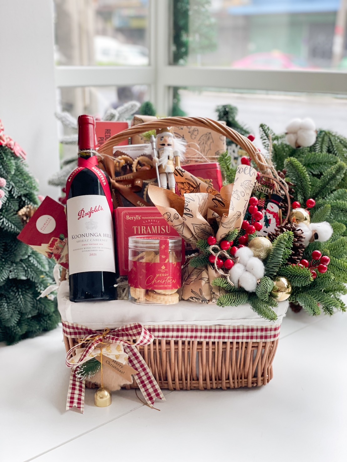 Luxurious holiday wicker hamper with premium wine, plum pudding, fruit mince pies, tiramisu biscuits, cookies, and festive ornaments.
