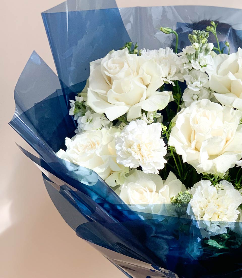 Close-up of a White rose bouquet with delicate white flowers, elegantly wrapped in navy blue paper and ribbon.