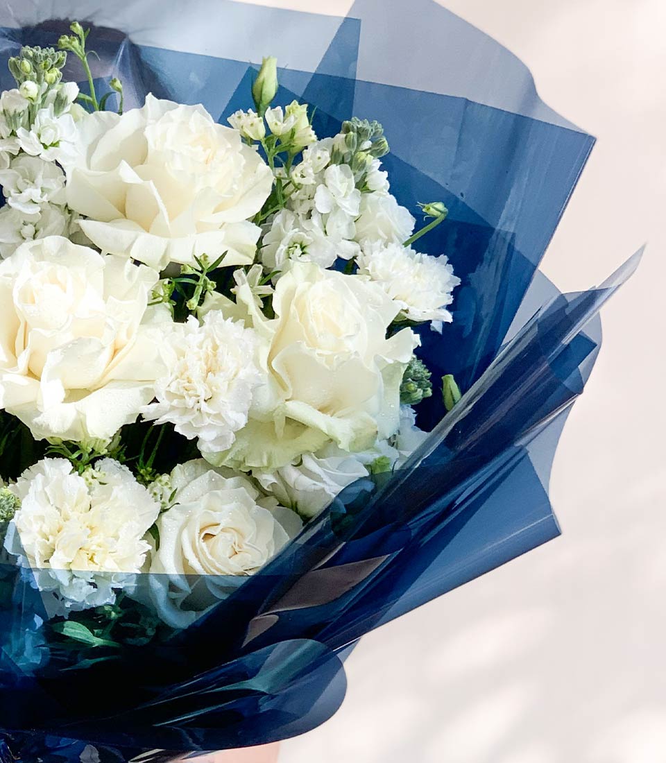 Close-up of a White rose bouquet with delicate white flowers, elegantly wrapped in navy blue paper and ribbon.