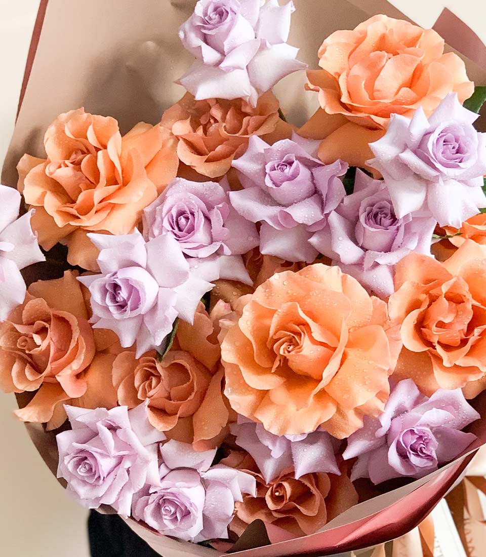 Close-up of a Bouquet of lilac and peach roses wrapped in soft brown paper with elegant ribbons.