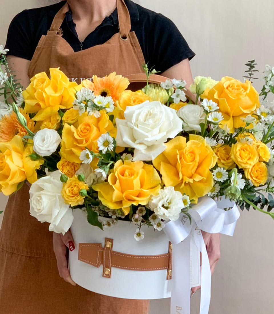 Luxury yellow and white flower arrangement in a round white box, held by a florist.