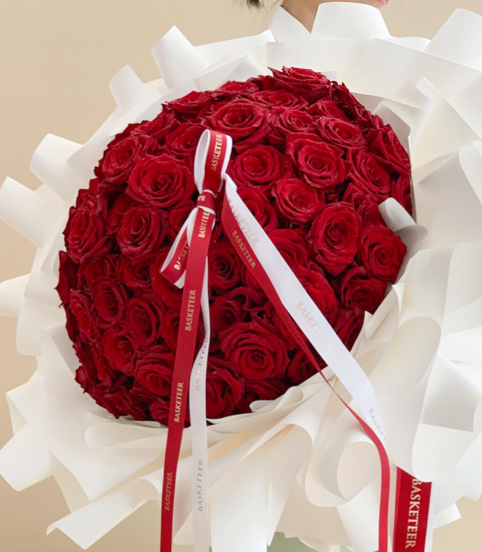 Close-up of a Heart-shaped bouquet of red roses with white ruffled wrapping and red and white ribbons.