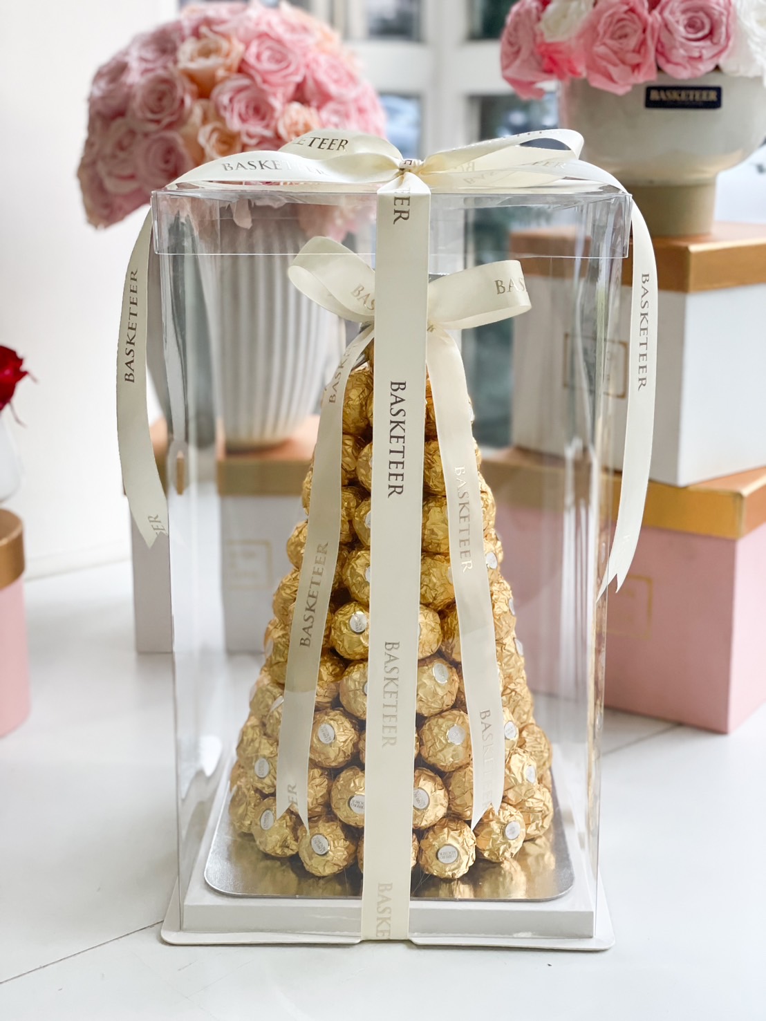 A beautifully arranged Ferrero Rocher Chocolate Tower, elegantly wrapped in a clear display box with Basketeer ribbons, making it a luxurious gift for any occasion.