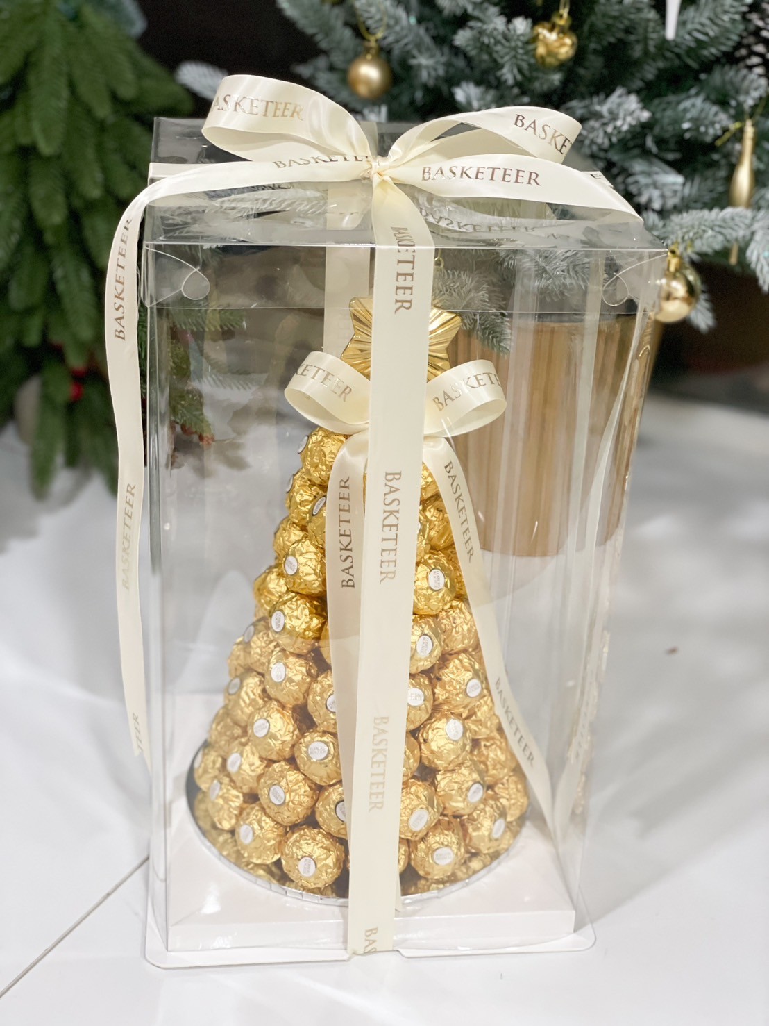 Golden Ferrero Rocher Christmas tree tower wrapped with Basketeer ribbon, presented in a clear box for a luxurious holiday gift.