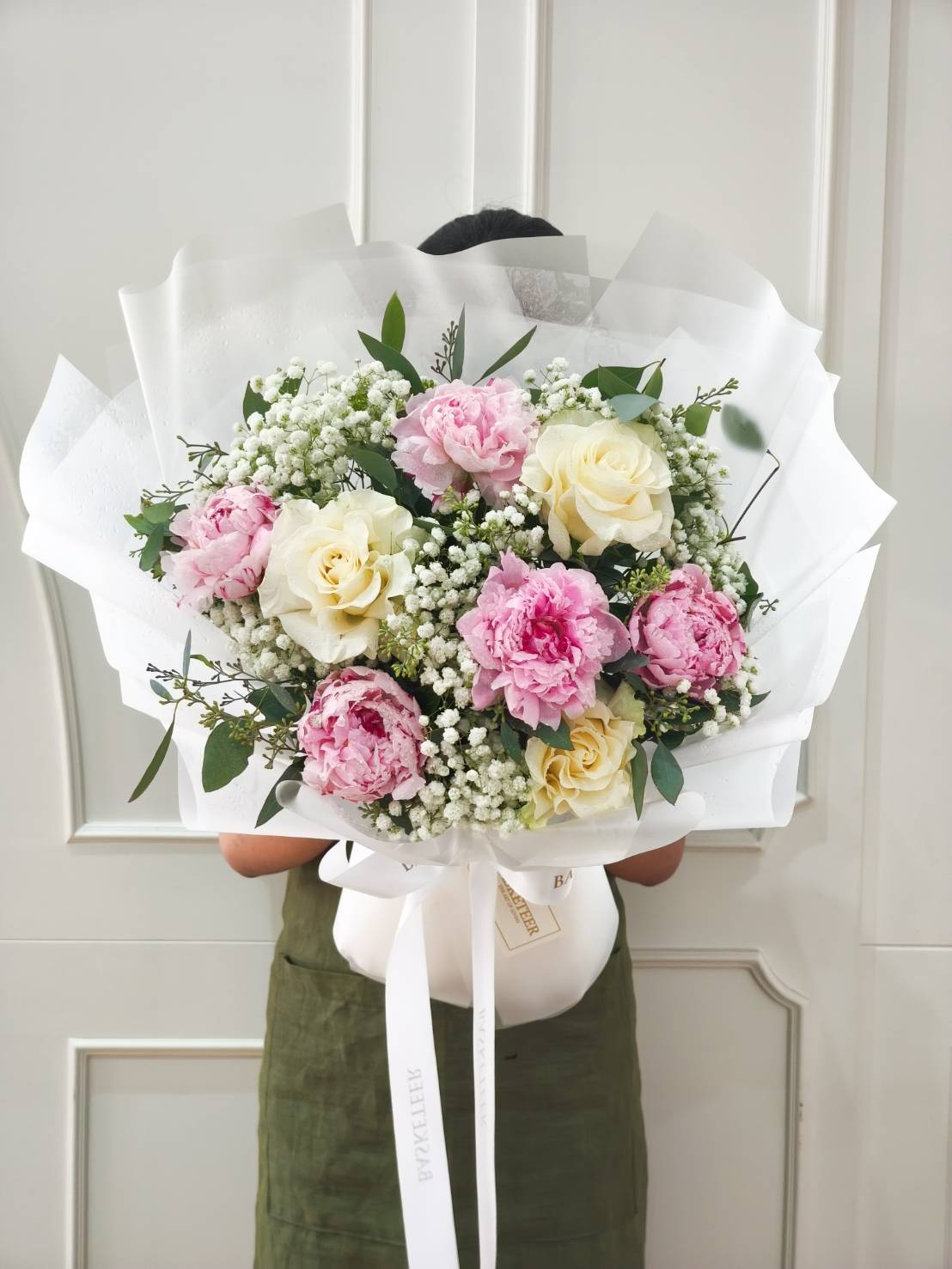Large bouquet of pink peonies, cream roses, and white baby’s breath wrapped in white paper.