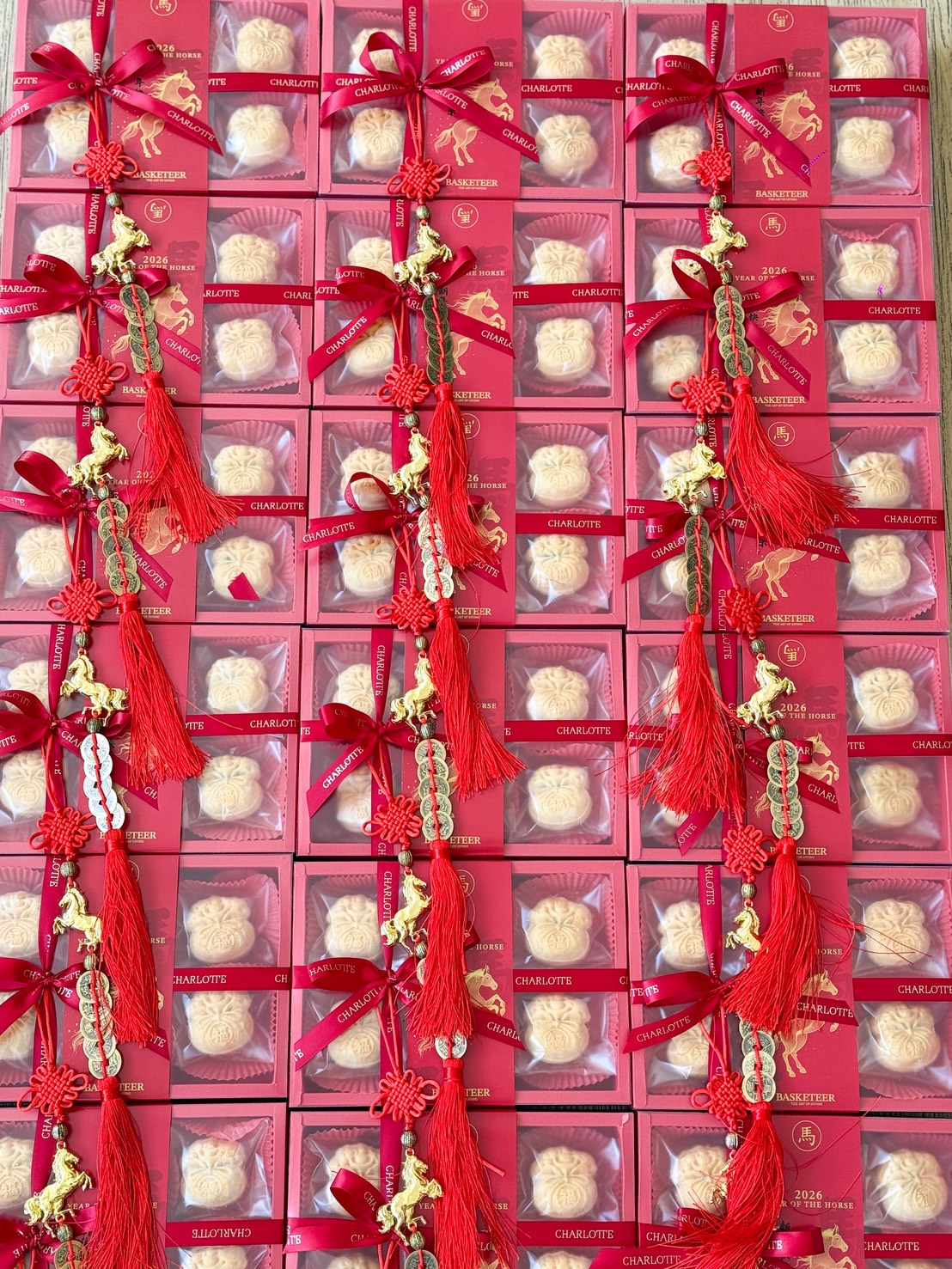 Boxes of mooncakes and Orange Cheese Tarts Gift with red packaging are arranged in a grid. Each box is tied with a red ribbon and topped with decorative red tassels and gold ornaments, creating a festive and vibrant display.