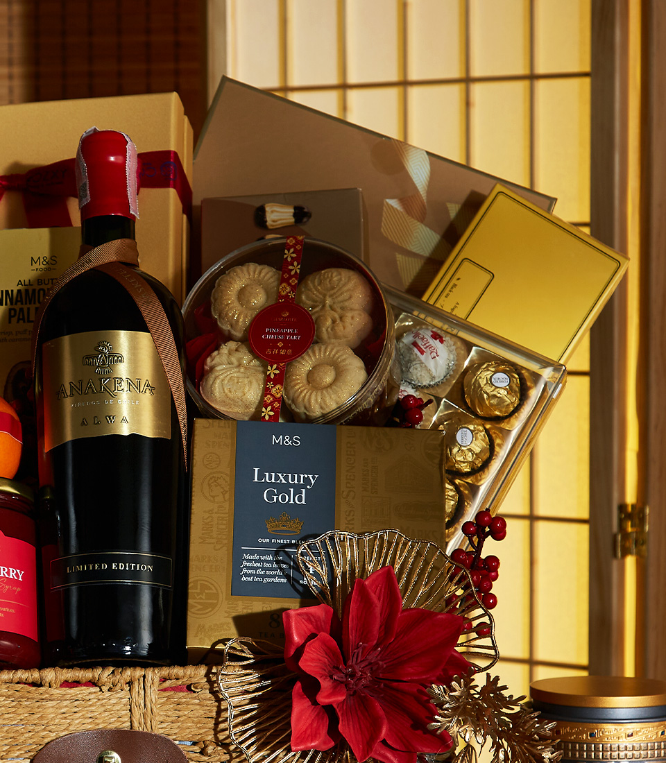 Close-up of a Elegant Chinese New Year gift basket with premium wine, cookies, oranges, and luxurious red and gold decorations.