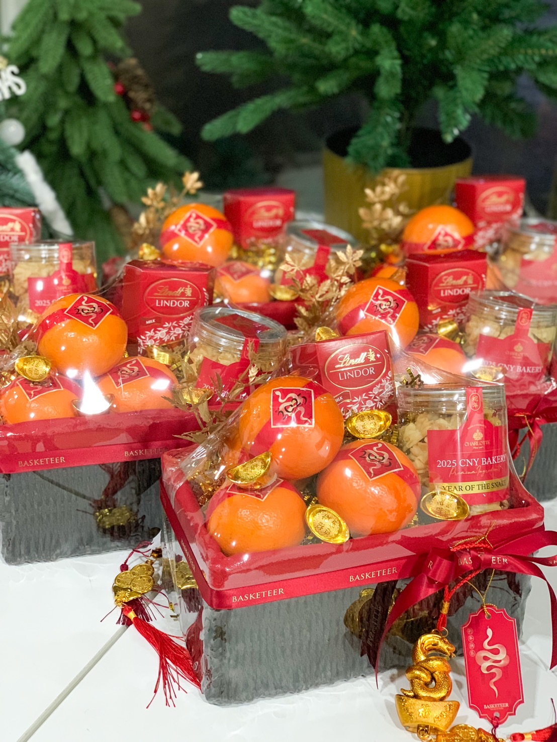 Close-up of a A collection of elegant Chinese New Year hampers featuring fresh oranges, golden charms, red festive ribbons, and premium gift items, ideal for the Year of the Snake celebrations.