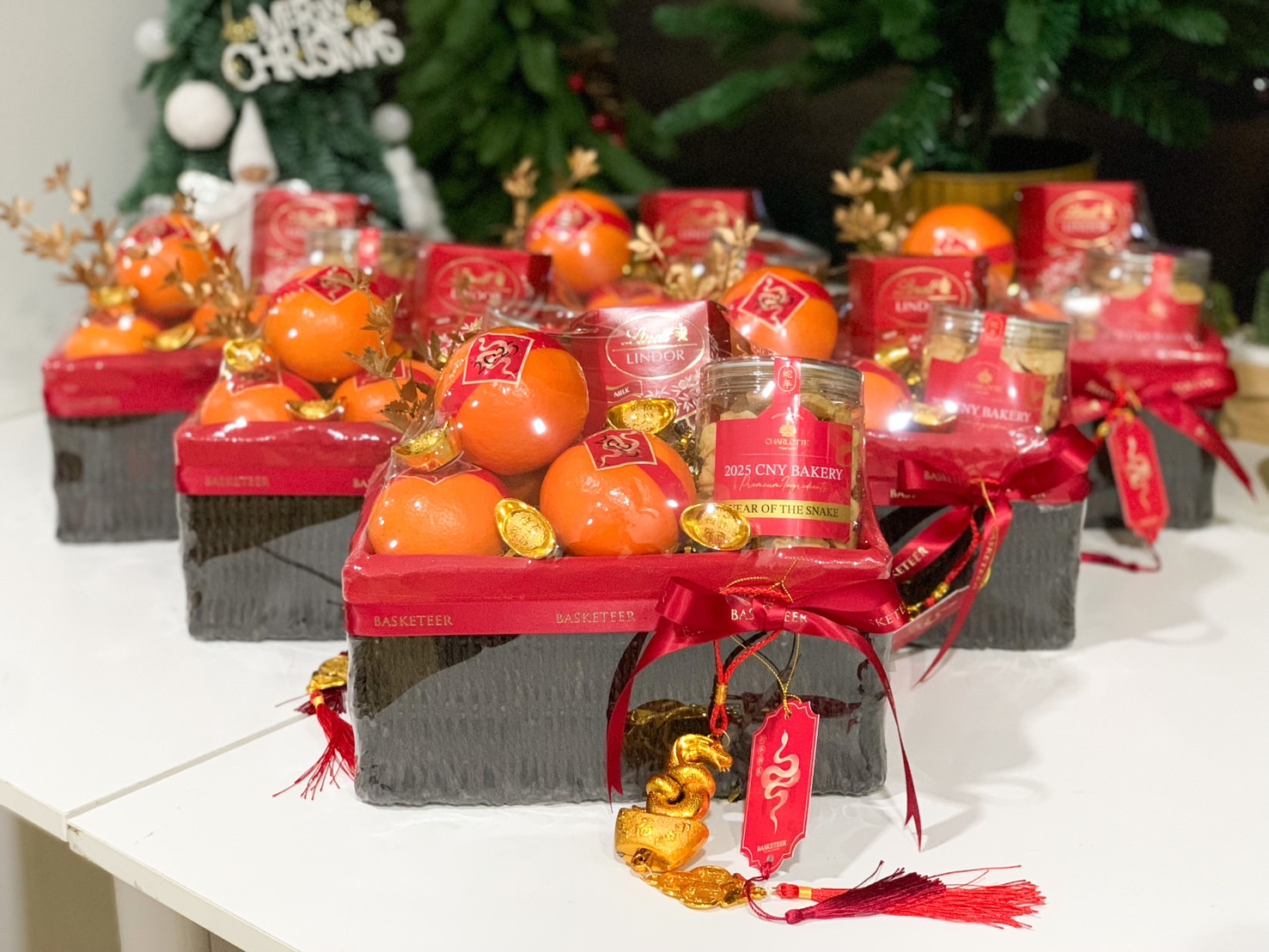 A collection of elegant Chinese New Year hampers featuring fresh oranges, golden charms, red festive ribbons, and premium gift items, ideal for the Year of the Snake celebrations.
