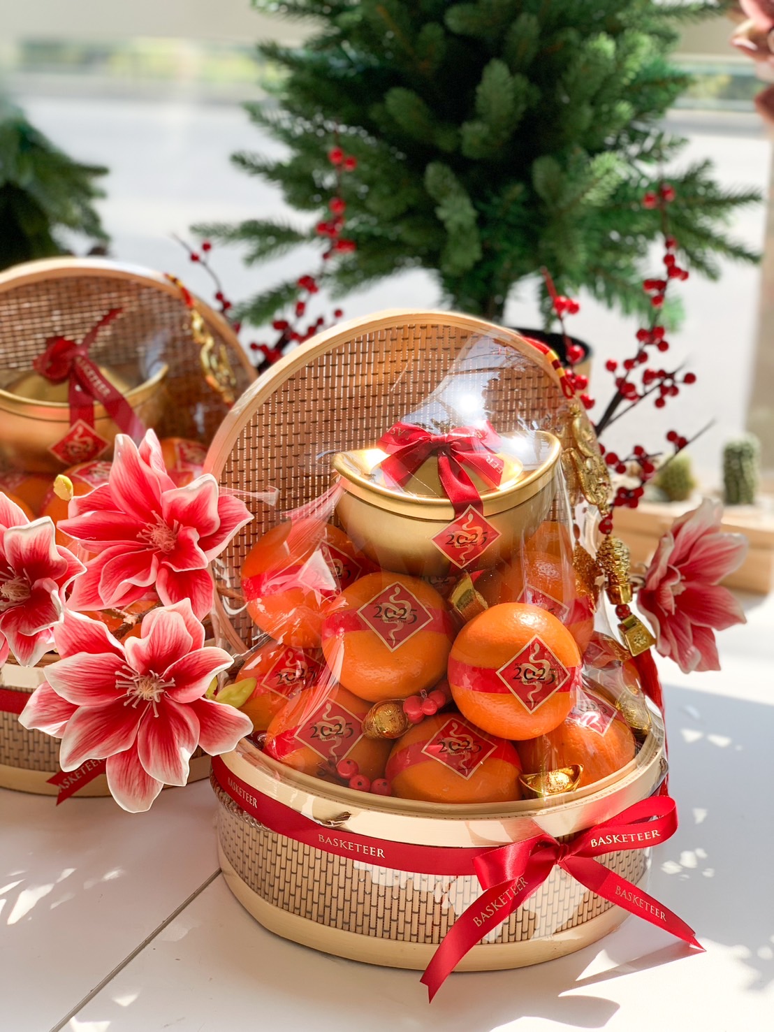 Elegant Chinese New Year basket with fresh mandarins, a gold ingot centerpiece, and adorned with red and gold flowers, wrapped in clear protective cover.