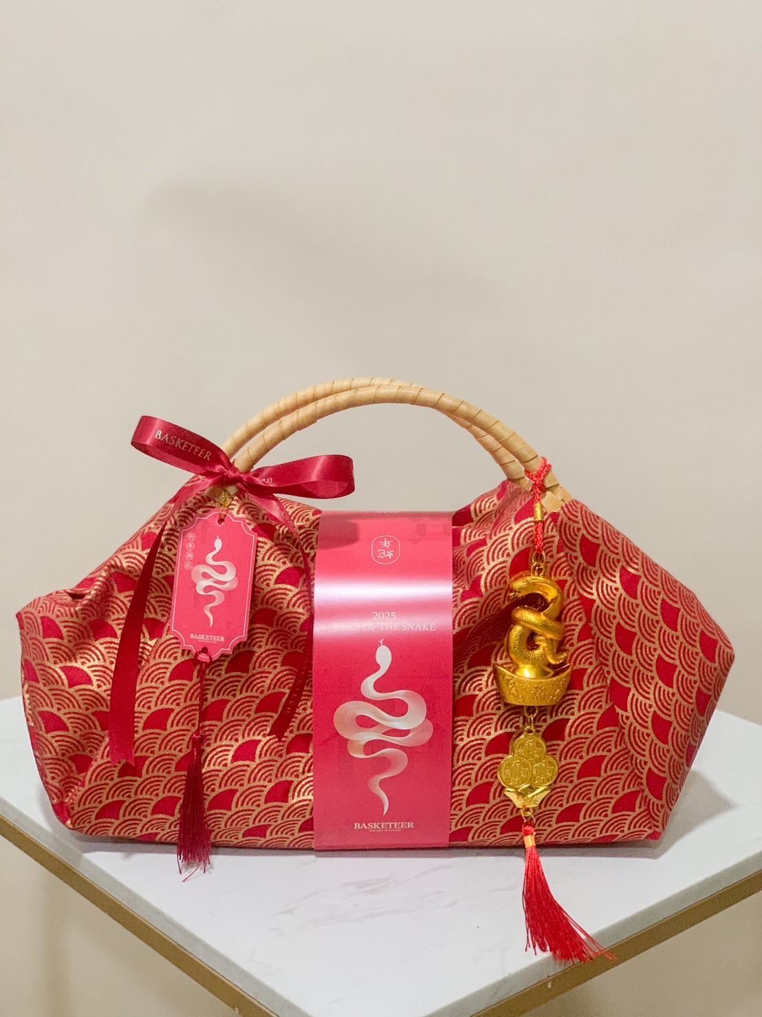 Red-wrapped tote basket with a wooden handle, adorned with a golden snake charm and festive ribbons, perfect for Chinese New Year gifting.
