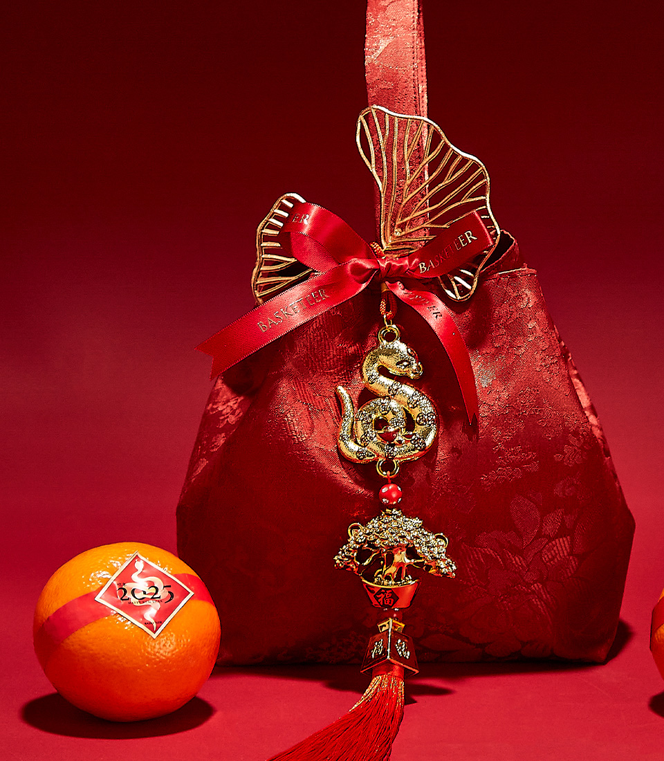 Close-up of a Red velvet bag with festive golden charms and a mandarin orange, symbolizing prosperity for Chinese New Year celebrations.