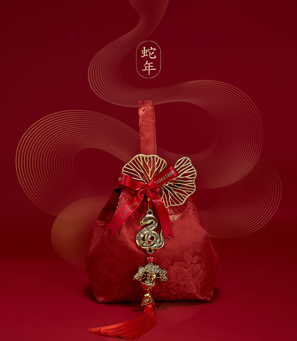 Red velvet bag with festive golden charms and a mandarin orange, symbolizing prosperity for Chinese New Year celebrations.