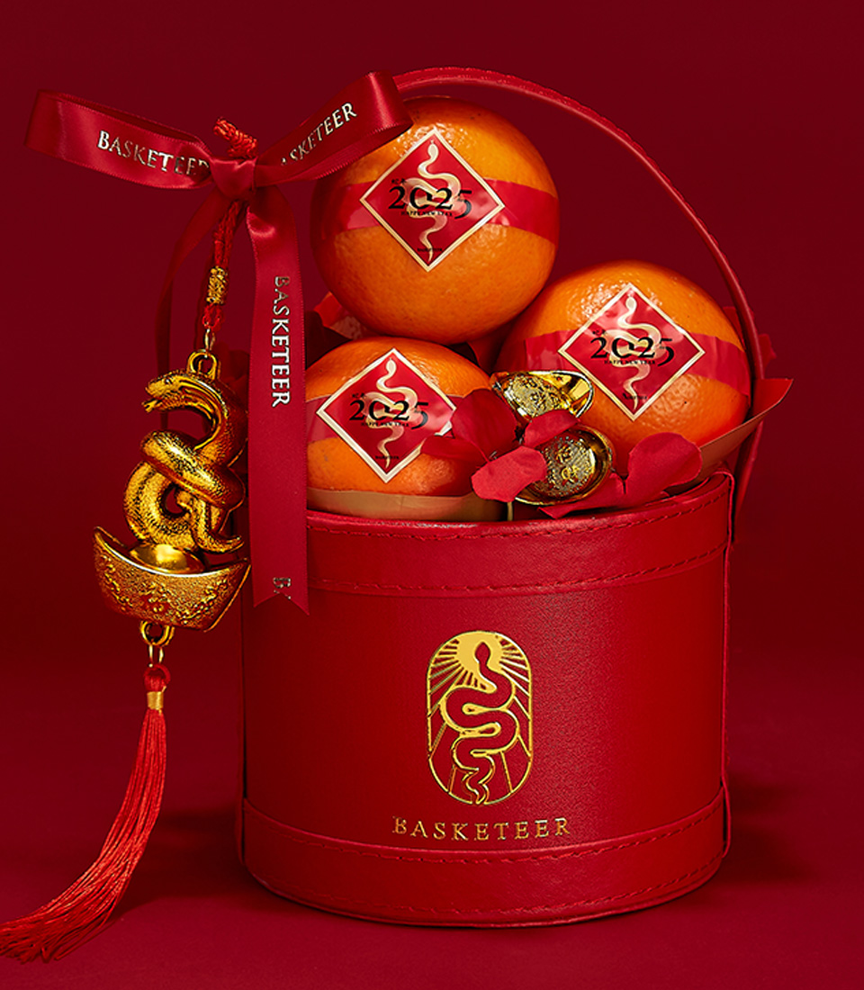 Close-up of a Red gift box featuring fresh mandarin oranges with gold accents and festive Chinese New Year decorations for the Year of the Snake.
