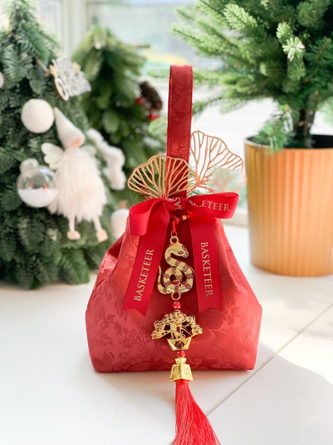 Red velvet bag with festive golden charms and a mandarin orange, symbolizing prosperity for Chinese New Year celebrations.