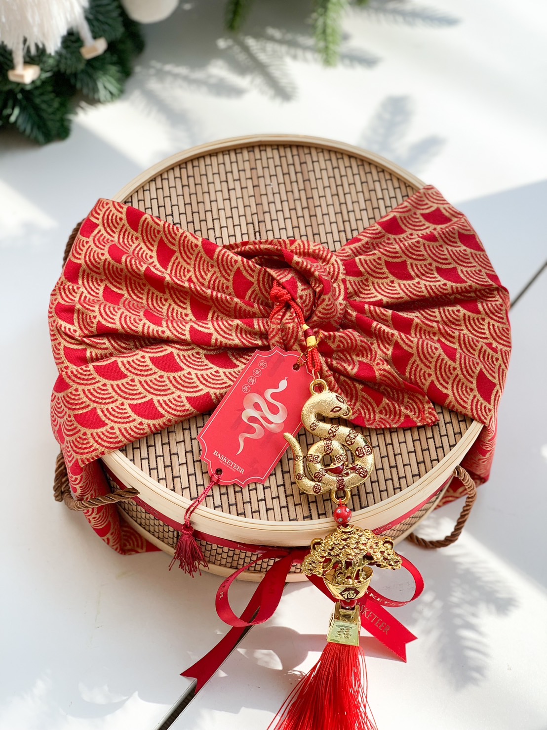 Bamboo gift basket adorned with red patterned wrap, snake charm, and festive ribbons for a perfect Chinese New Year gift.