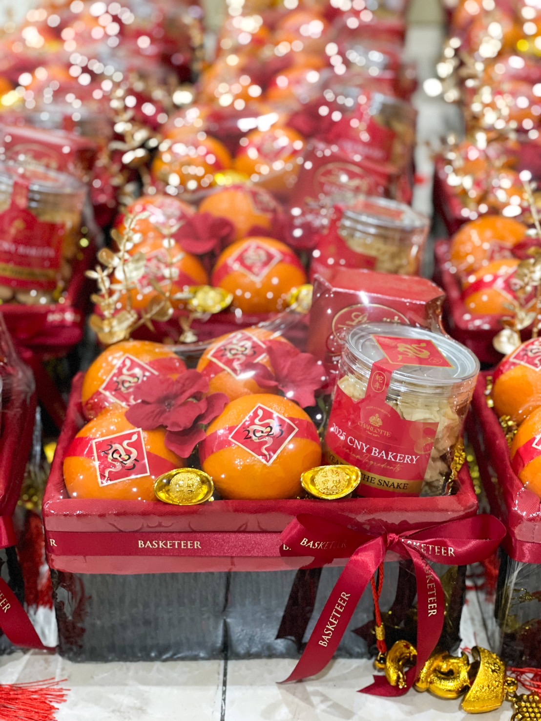 Lunar New Year gift basket featuring fresh oranges, festive cookies in a jar, golden coins, and decorative red ribbons.
