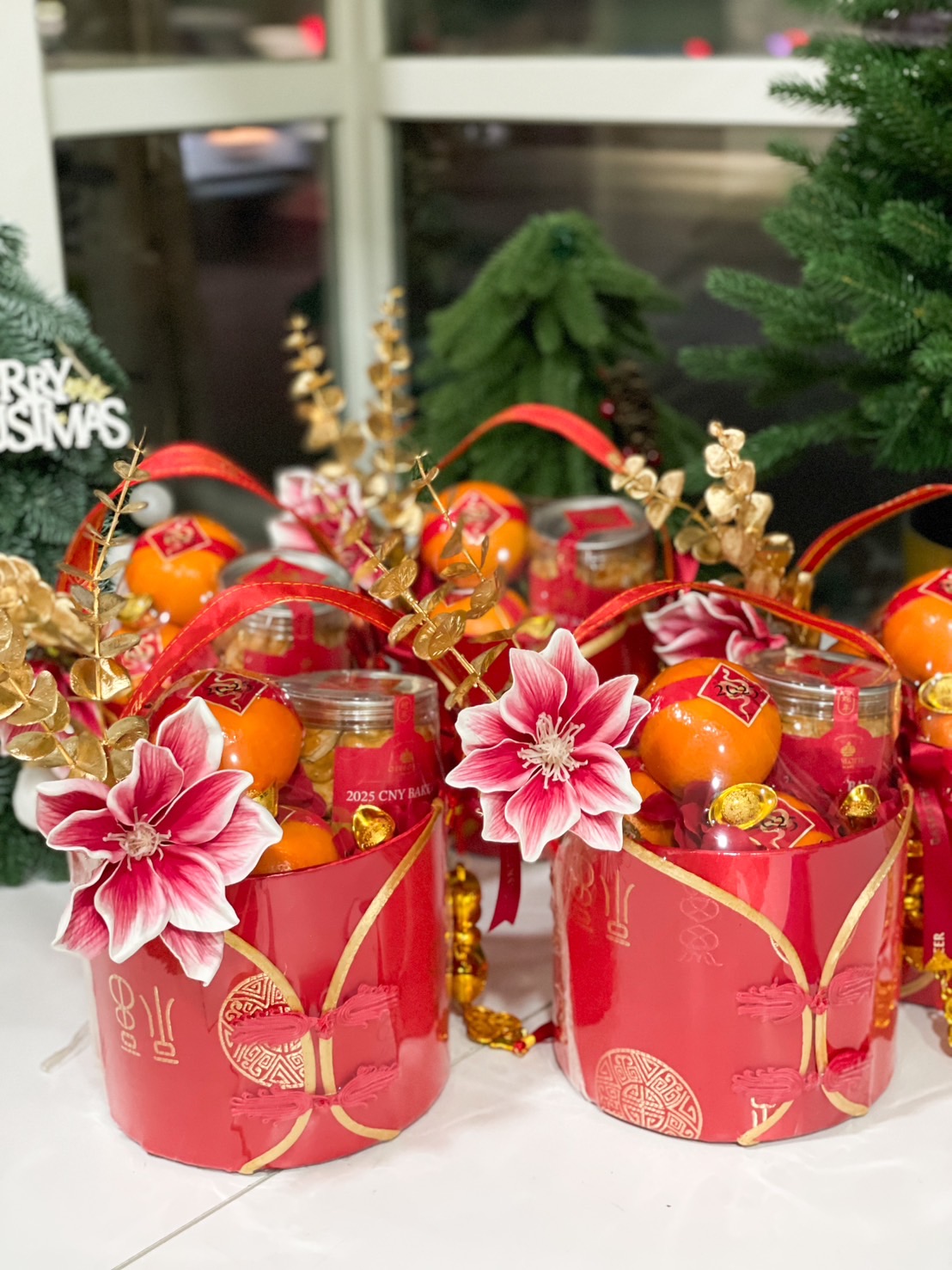 Chinese New Year gift basket with fresh oranges, cookies in a jar, golden coins, red ribbons, and floral decorations in a red festive container.