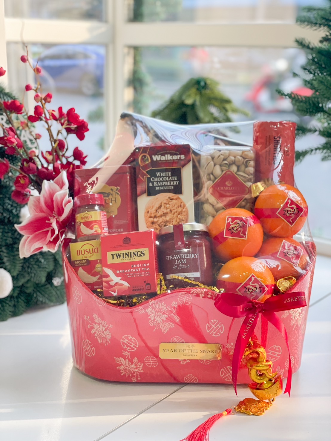 Red gift hamper for Year of the Snake with Twinings tea, Walkers white chocolate biscuits, strawberry jam, oranges, and festive embellishments.