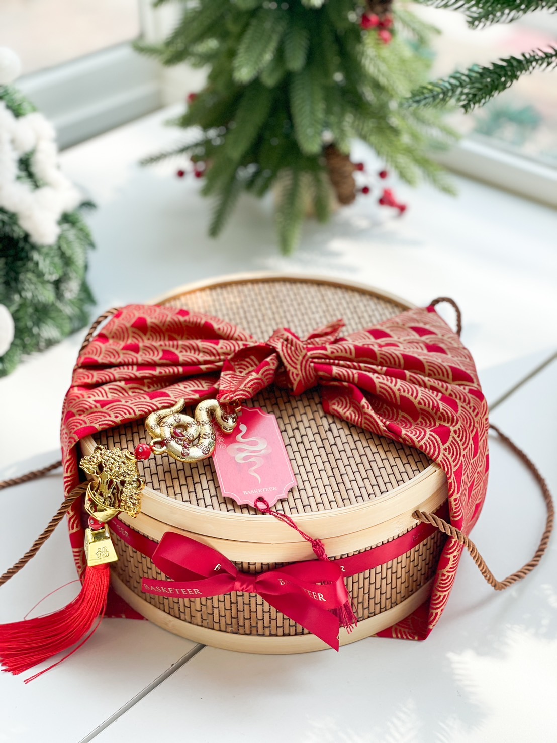 Bamboo gift basket adorned with red patterned wrap, snake charm, and festive ribbons for a perfect Chinese New Year gift.