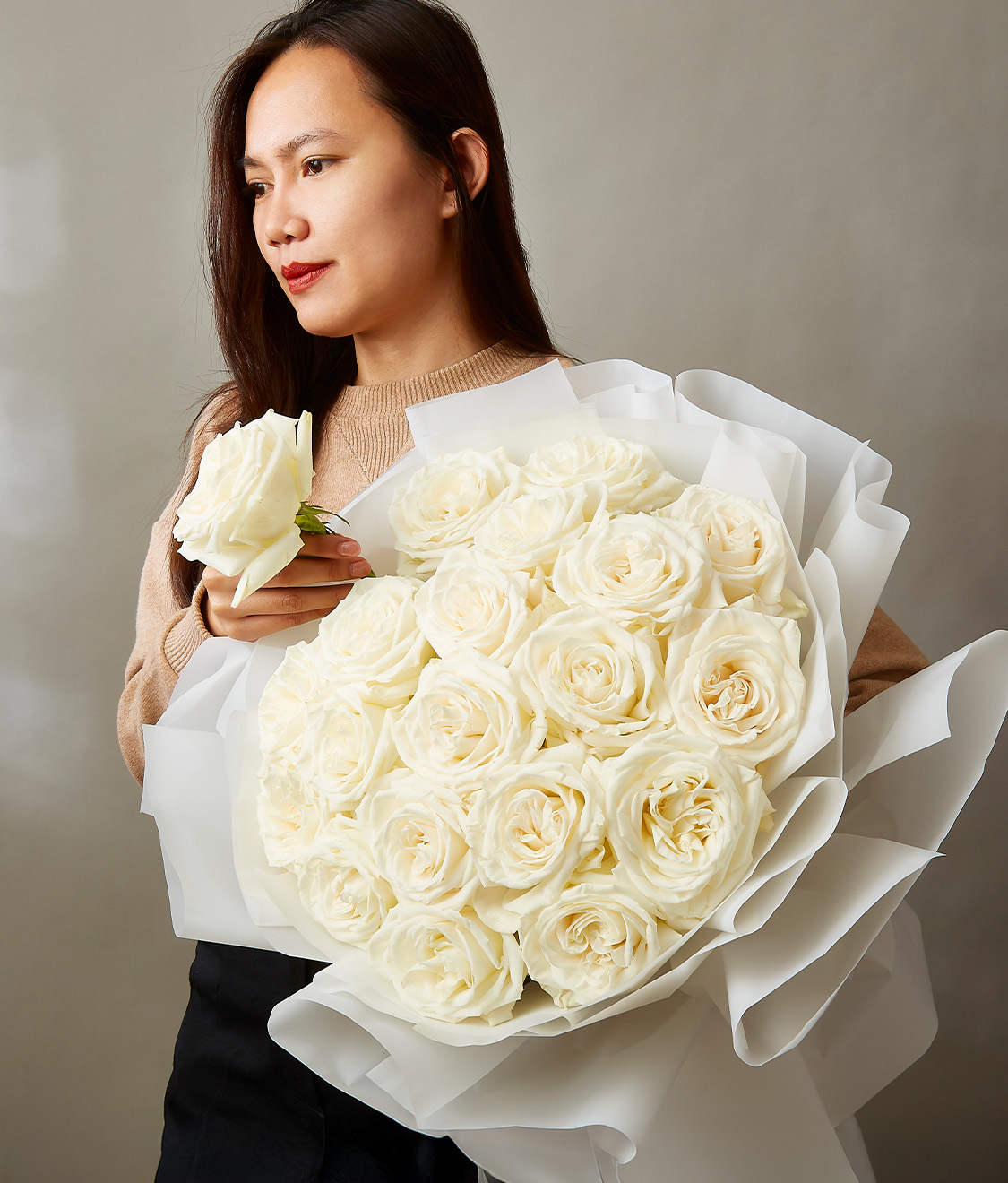 A woman holding an elegant bouquet of fresh white roses, wrapped in soft white paper, symbolizing purity and grace.