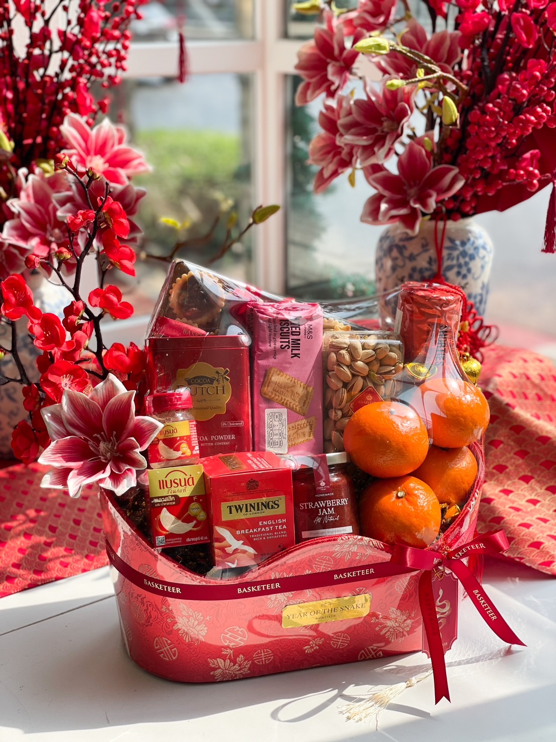 A luxurious Chinese New Year gift hamper filled with premium mandarin oranges, gourmet snacks, tea, and festive decorations in a red and gold gift box.
