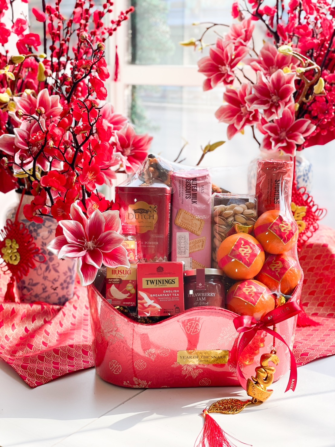 A luxurious Chinese New Year gift hamper filled with premium mandarin oranges, gourmet snacks, tea, and festive decorations in a red and gold gift box.
